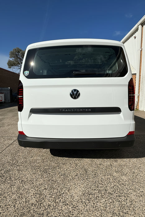 White Volkswagen t7 Transporter van parked on a concrete surface with a clear blue sky.